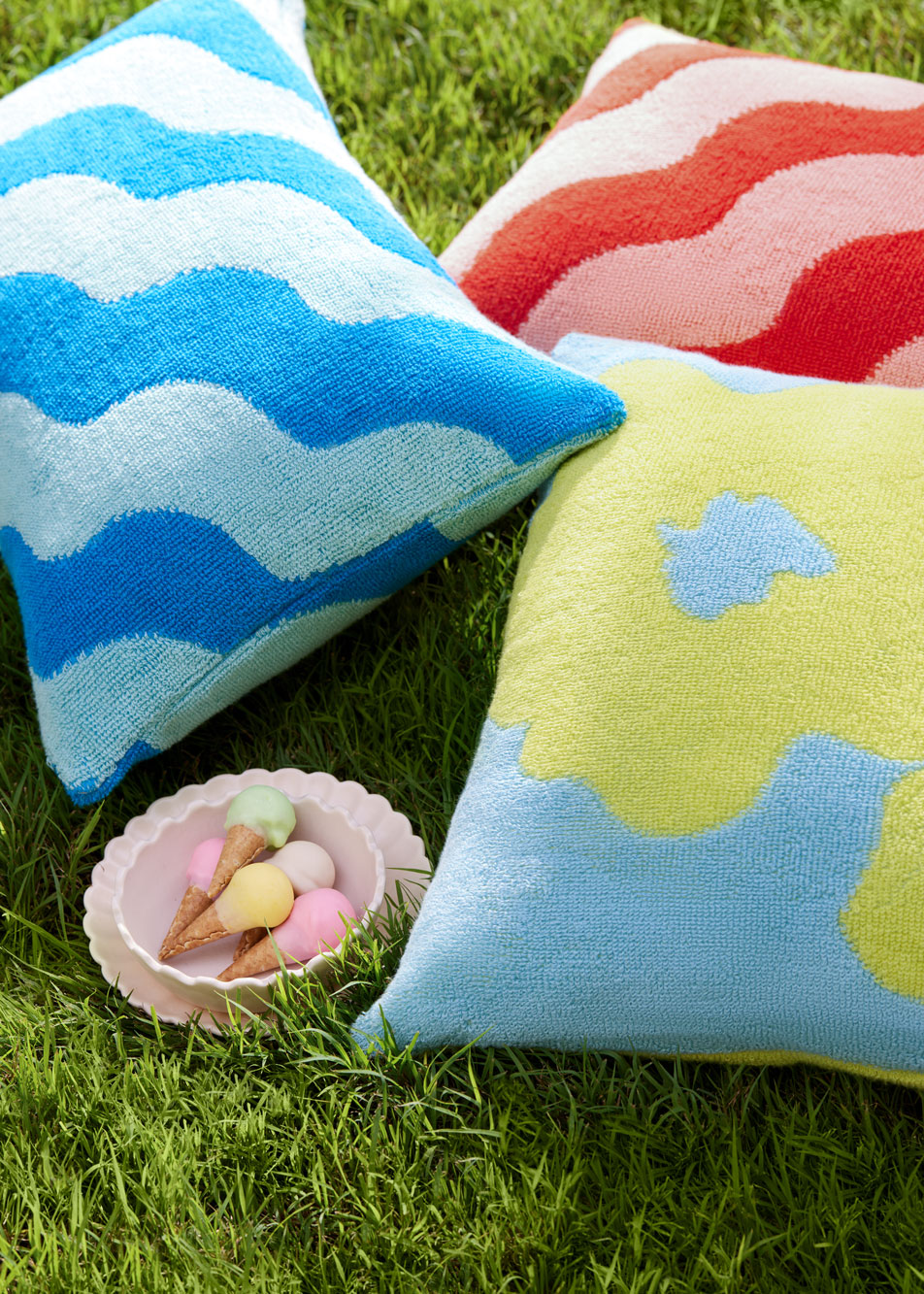 Three outdoor cushions sitting on grass next to a bowl of lollies