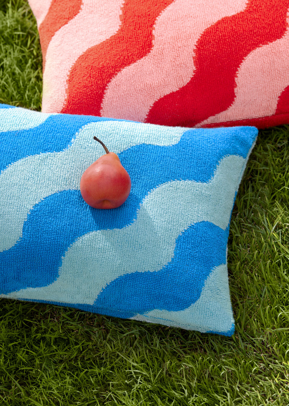 Two outdoor cushions laying on the grass. A red pear sits on top of one.