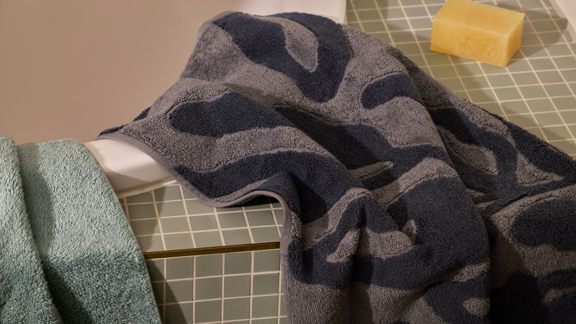 Two Sheridan bath towels draped over the side of a tiled bath tub