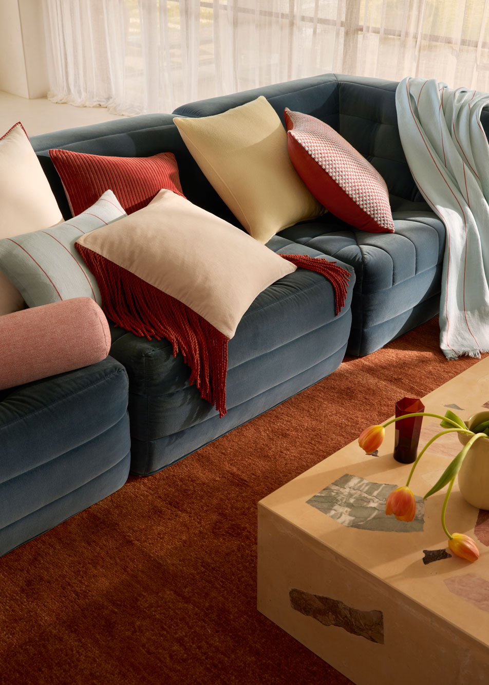 A blue velvet lounge styled with cushions in assorted colours and shapes