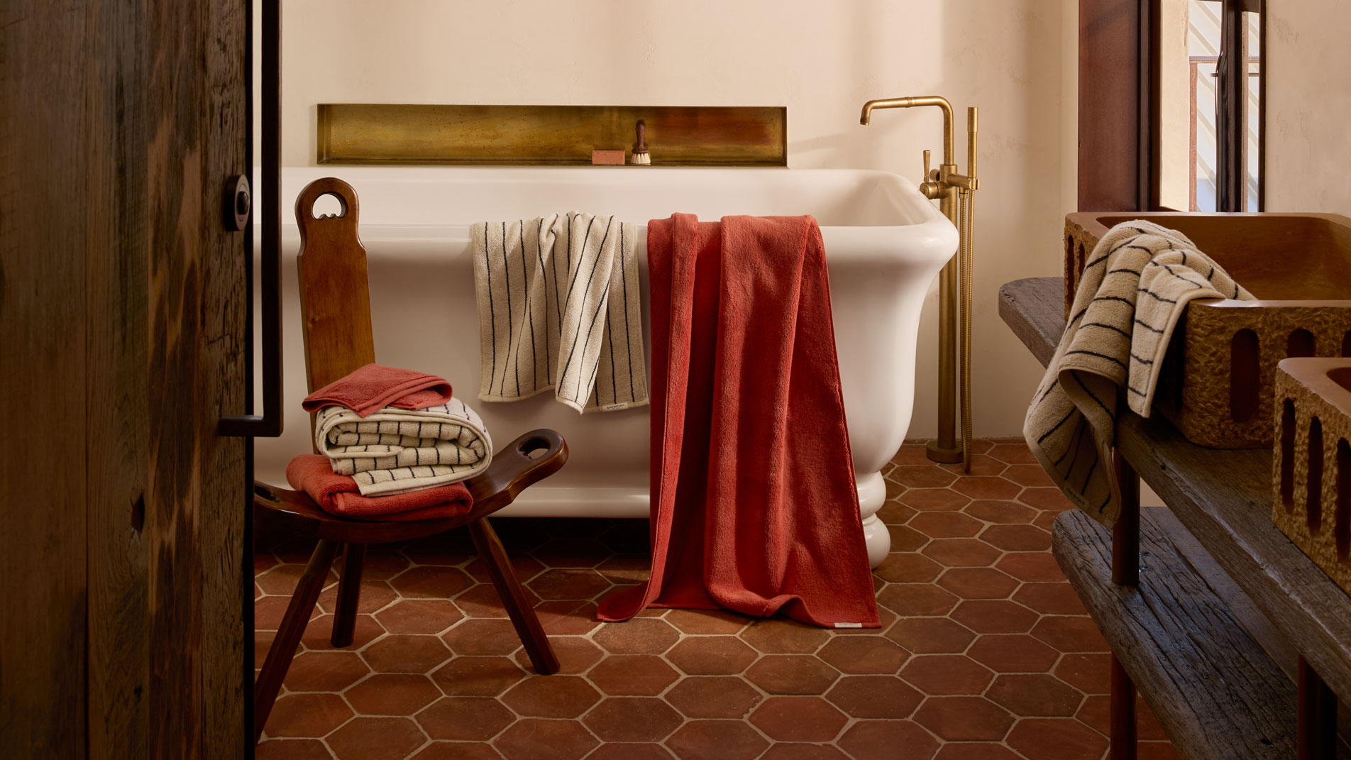 Aven bath towels in relish and limestone stripe draped over the side of a white porcelain bath tub