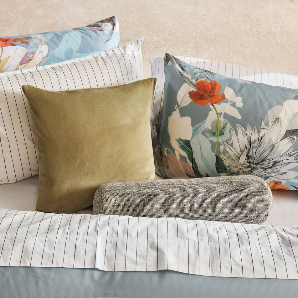 A floral print bed with one green cushion and one grey bolster