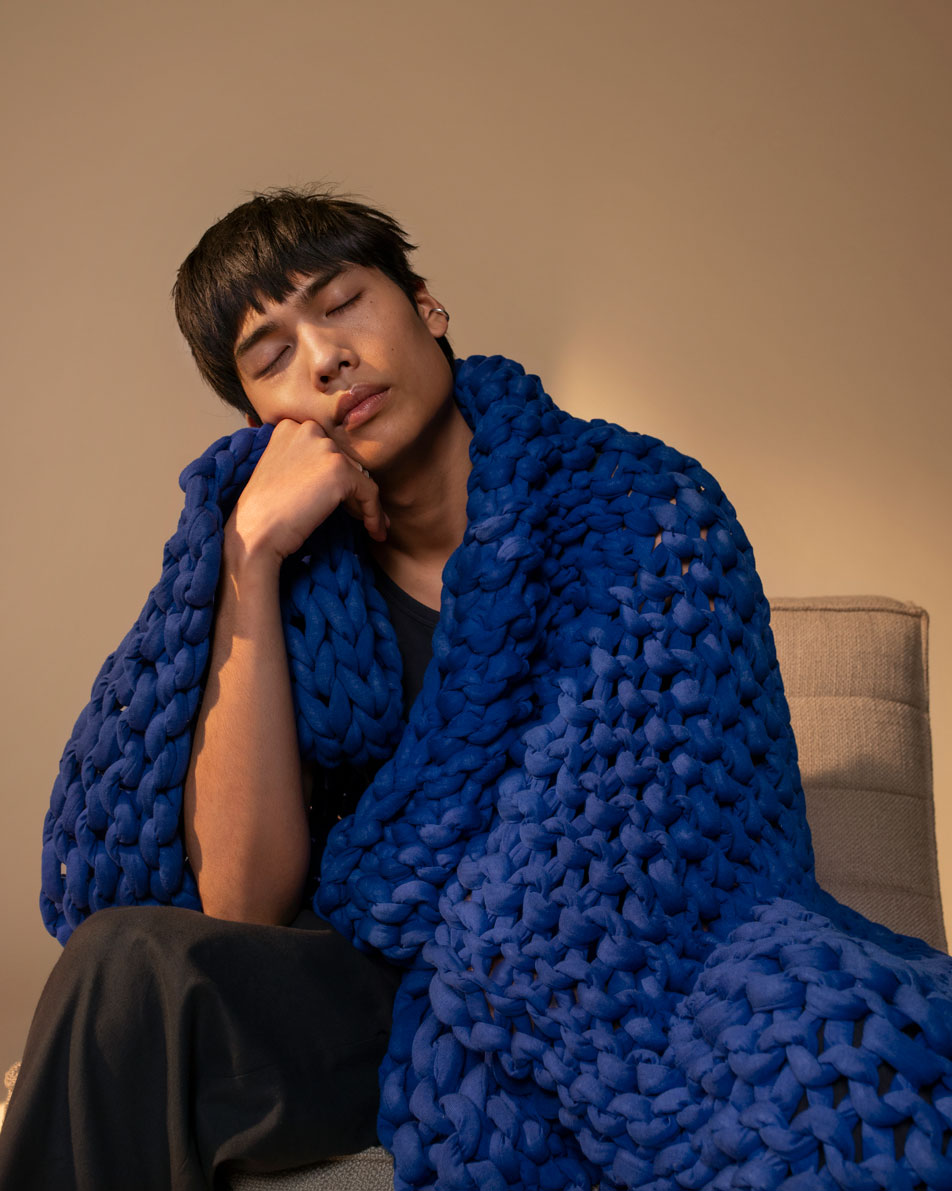 A young man resting his chin on his hand, sitting wrapped in a blue weighted blanket