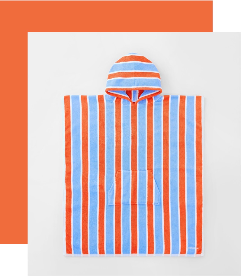 styled flat lay. blue, orange-red and white striped poncho shot from above. a thick red border goes around one corner and two sides.