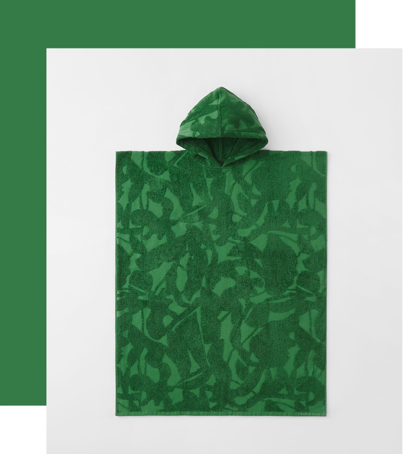 styled flat lay. palm green hooded poncho shot from above. a thick green border goes around one corner and two sides.