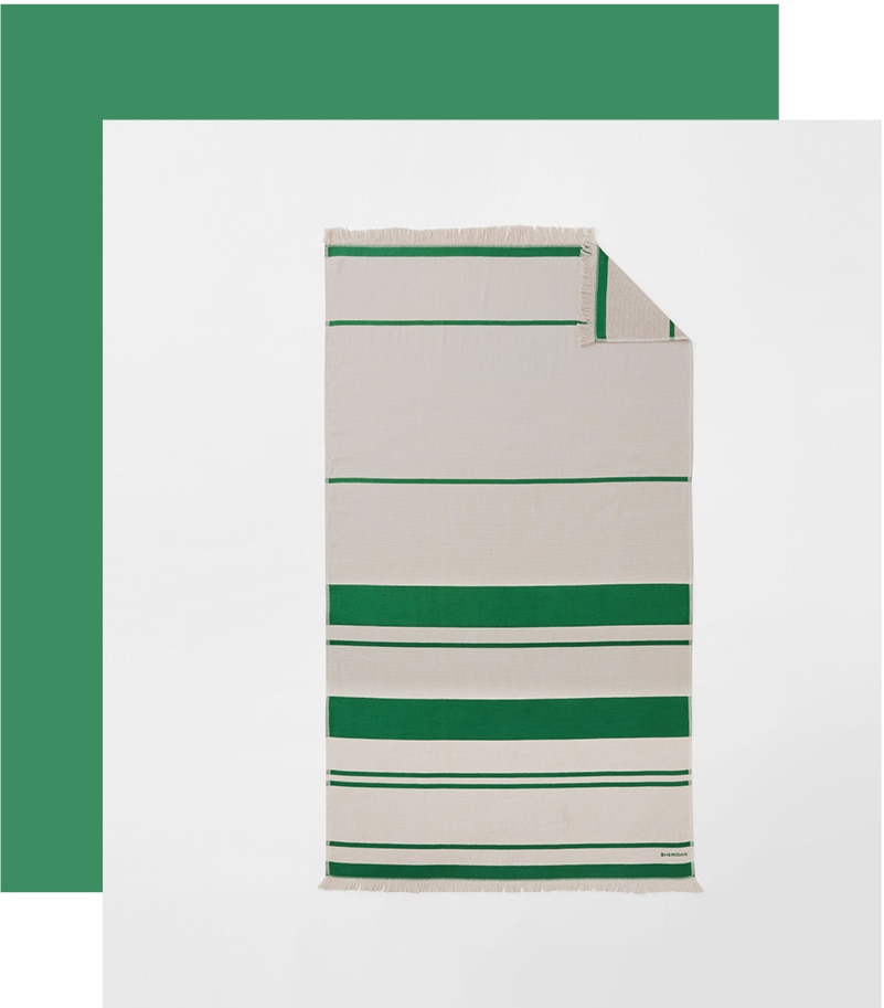 styled flat lay. flax and palm green striped beach towel shot from above. a thick green border goes around one corner and two sides.