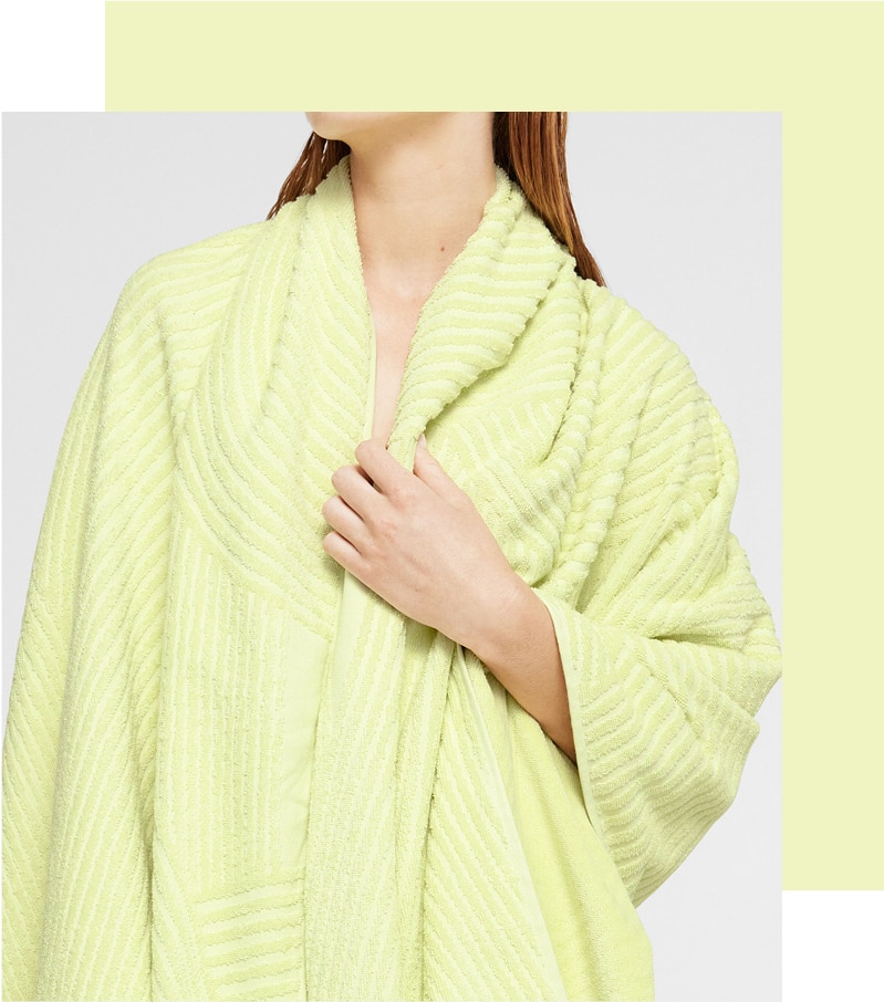 citrus lime yellow towel with high-low textured effect is draped round the shoulders of a white woman with red hair. she holds the towel closed at her front. a thick border of same colour goes around one corner and two sides.