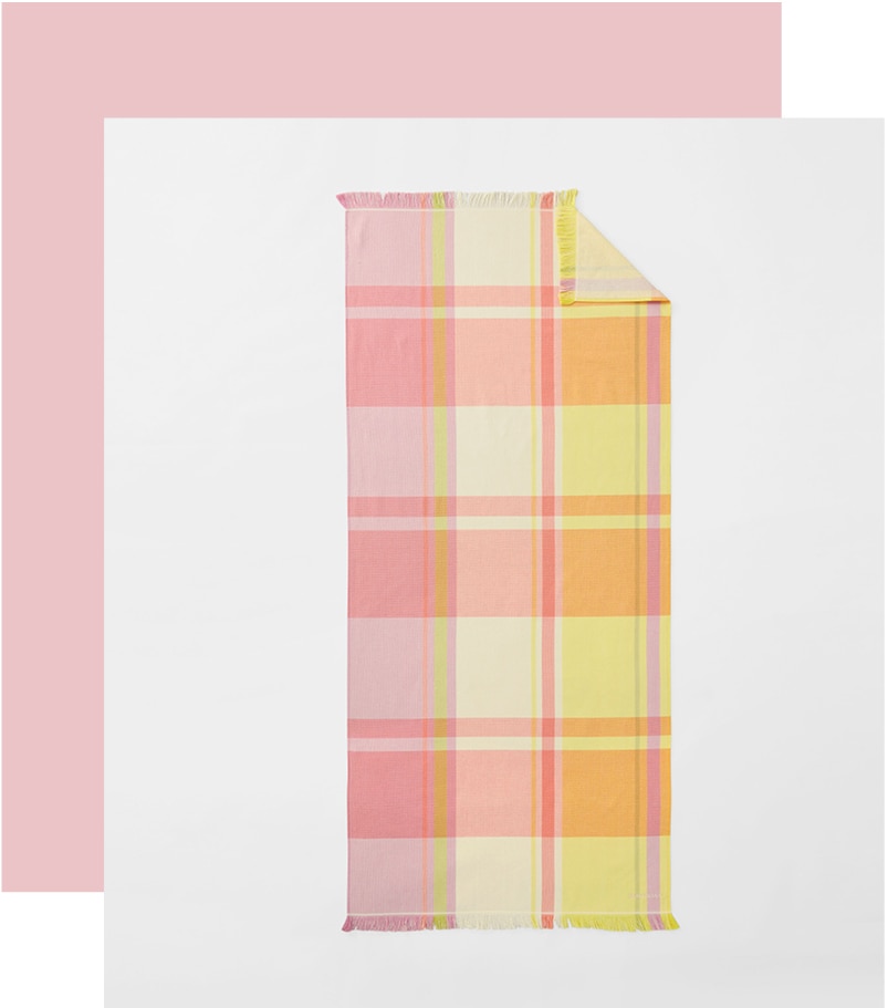 styled flat lay. multi-coloured check beach towel, in light summer yellows of yellow, orange, pink. a thick pink border goes around one corner and two sides.