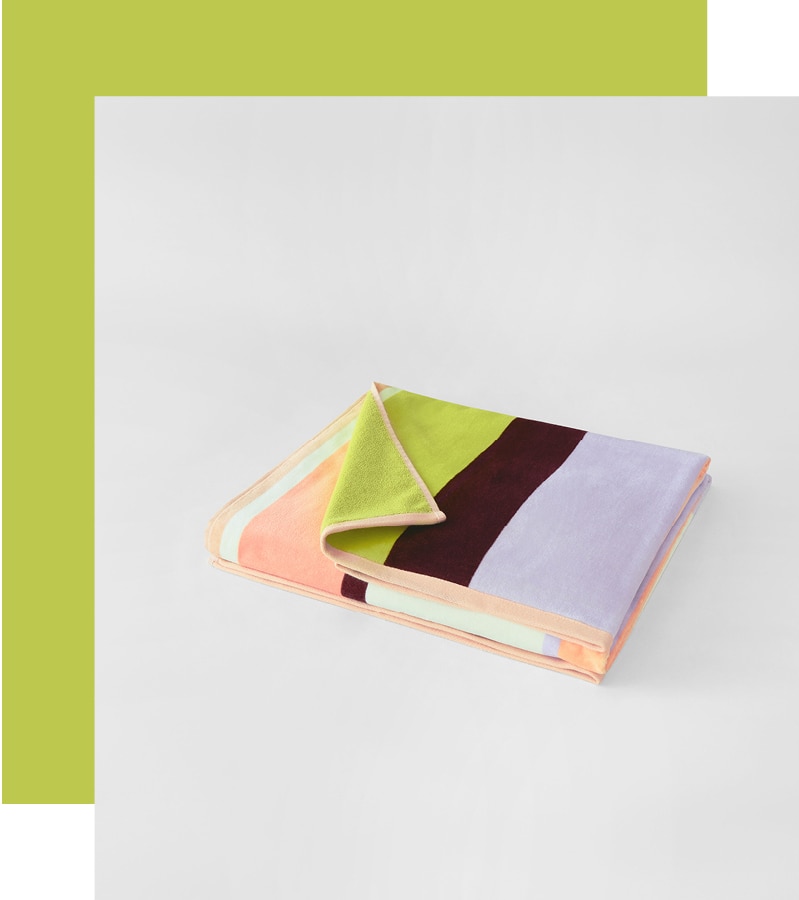 styled flat lay. multi-coloured striped beach towel folded, and shot from diagonally upwards. a thick lime-green border goes around one corner and two sides.