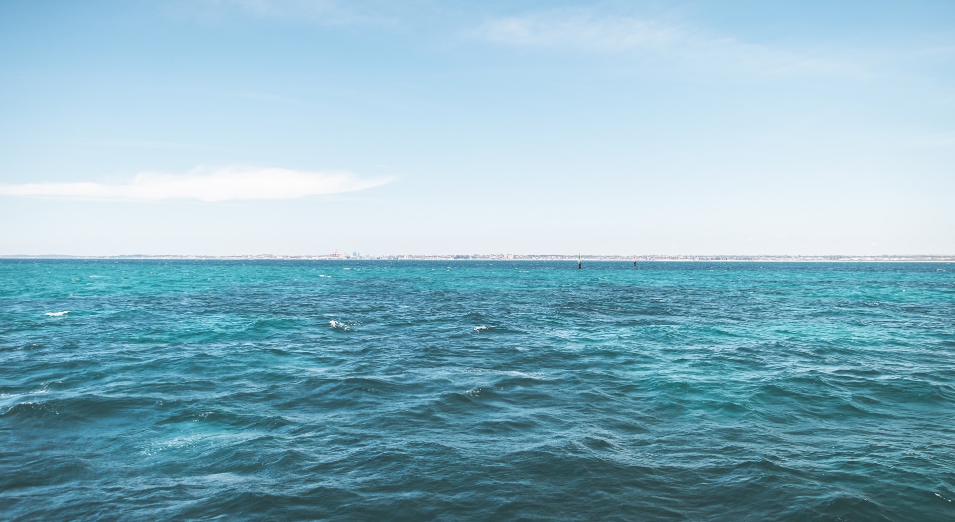 sleep strategies. calming shot of ocean, taken in the sea. half the image is vivid blue water with gentle ripples, other half is blue sky with lazy white clouds floating across.