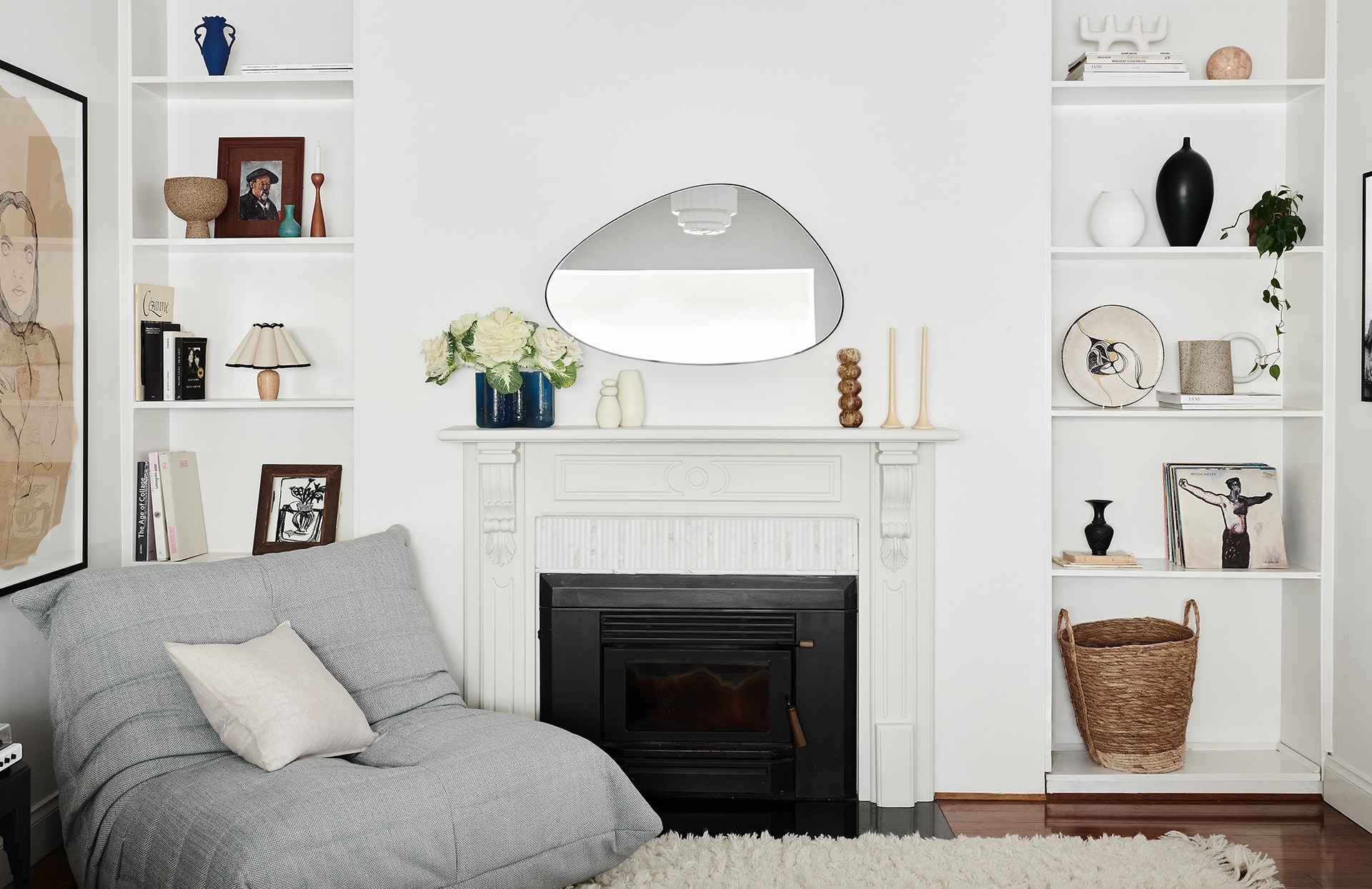 classic white living room. in middle is black fireplace with painted white wooden feature. grey lounge on corner has sheridan abbotson flax cushion. shelves on either side contain various knick-knacks.