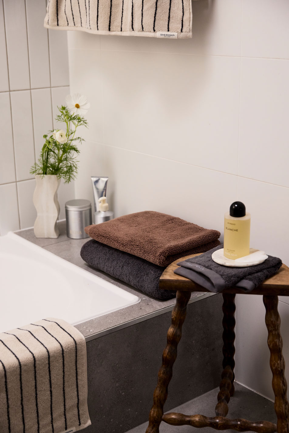 Various Sheridan towels folded and arranged beside a bathtub