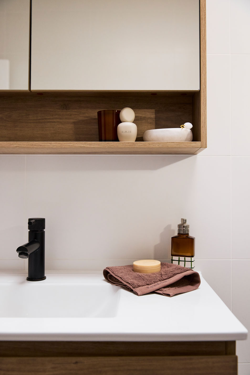 A white bathroom sink with a folded Sheridan hand towel on top, next to the hand towel is a bottle of perfume and a bar of soap