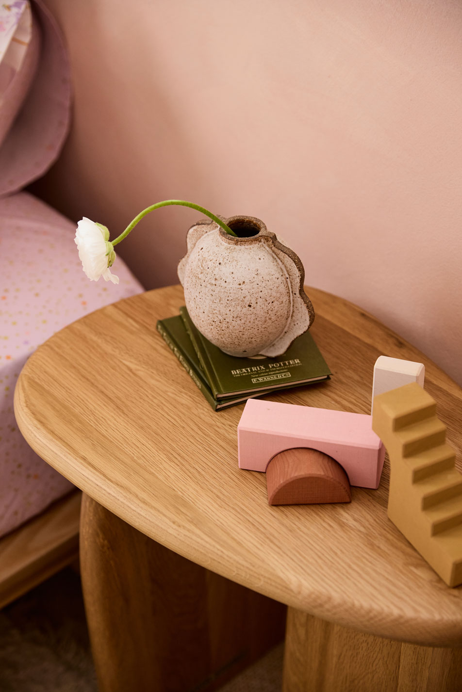 A side table in a children's bedroom. On top of the table is a vase and various toys.