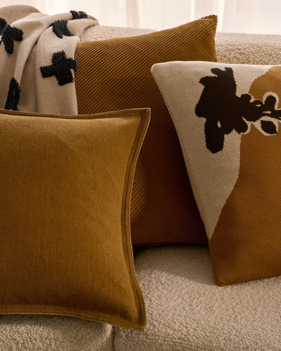 A close-up image of three cushions and a throw on a cream boucle sofa. The cushions are different designs all in the colour cardamon.