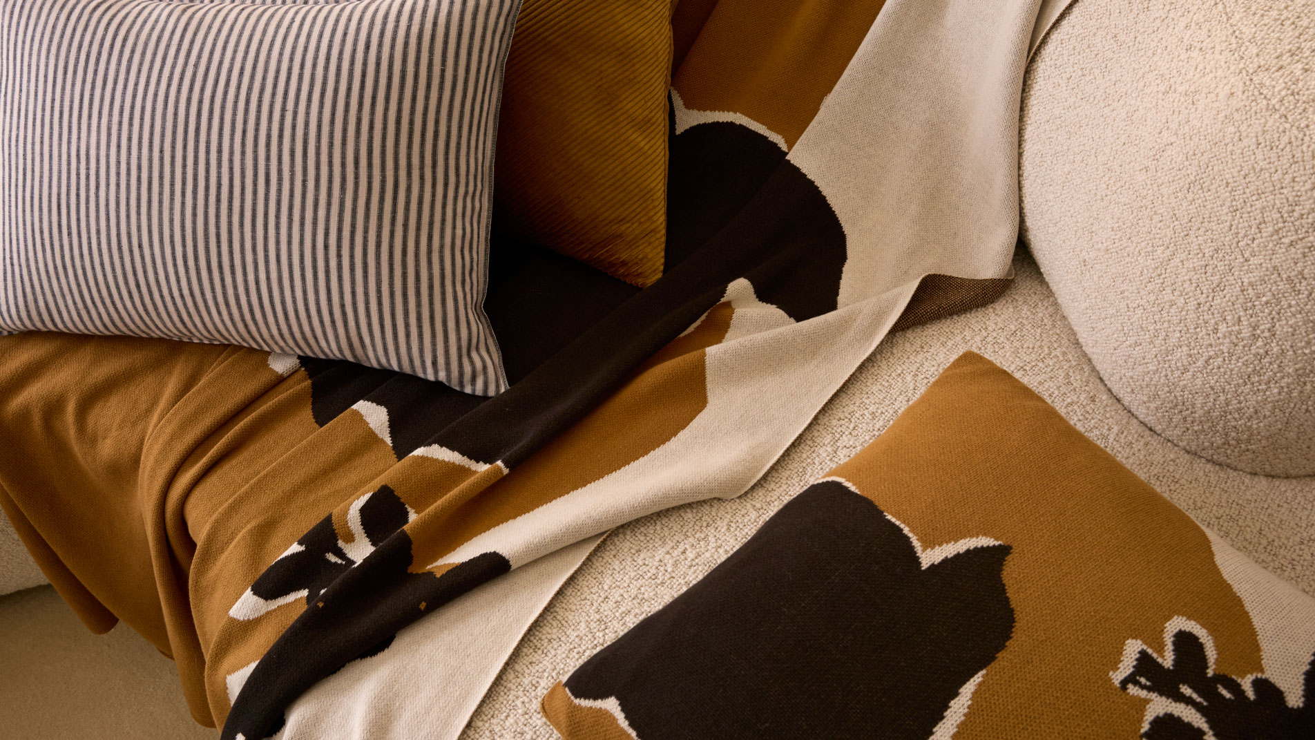 A close-up of a Perez Throw and Perez Flora Cushion on a cream boucle sofa.