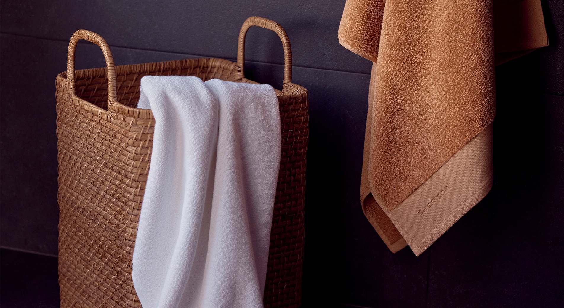 white towel in woven basket, orange towel hanging from wall.