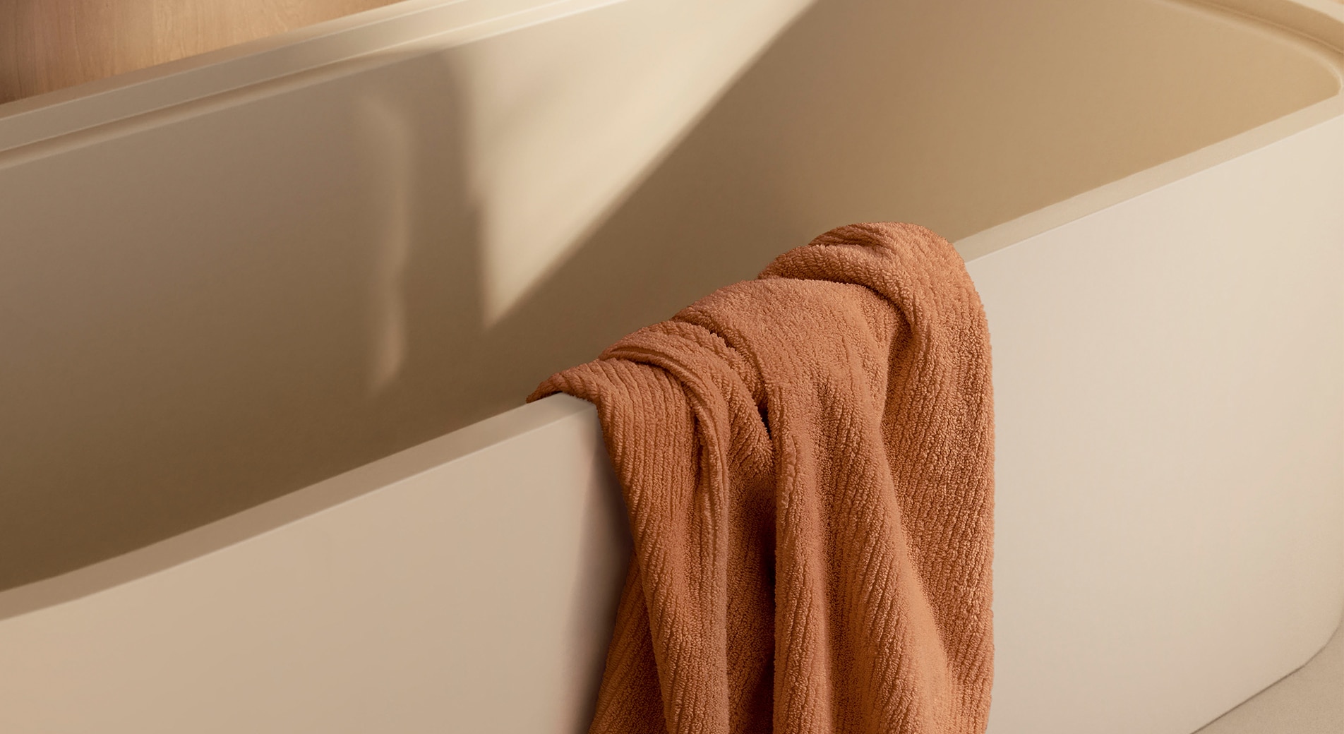 orange towel is styled over the side of a cream bath tub.