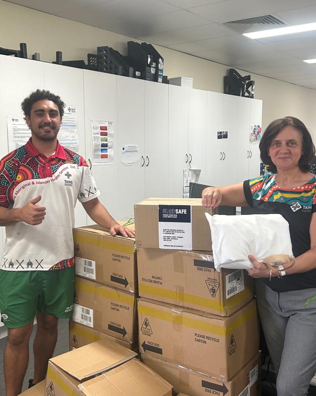 Two frontline homelessness workers standing either side of stacked cardboard boxes, full of SleepSafe sleep kits