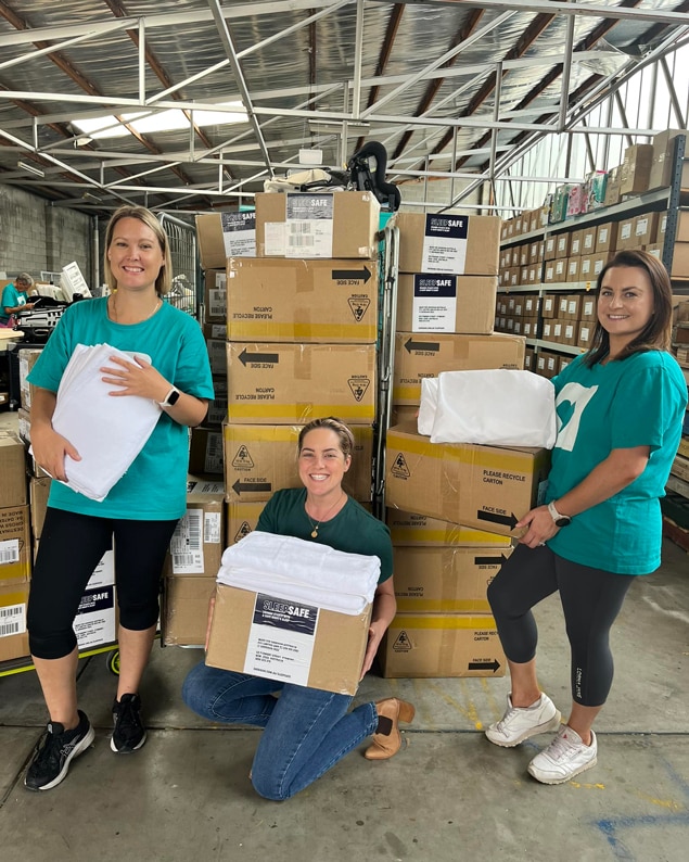 Three frontline homelessness workers in a warehouse with boxes full of SleepSafe sleep kits
