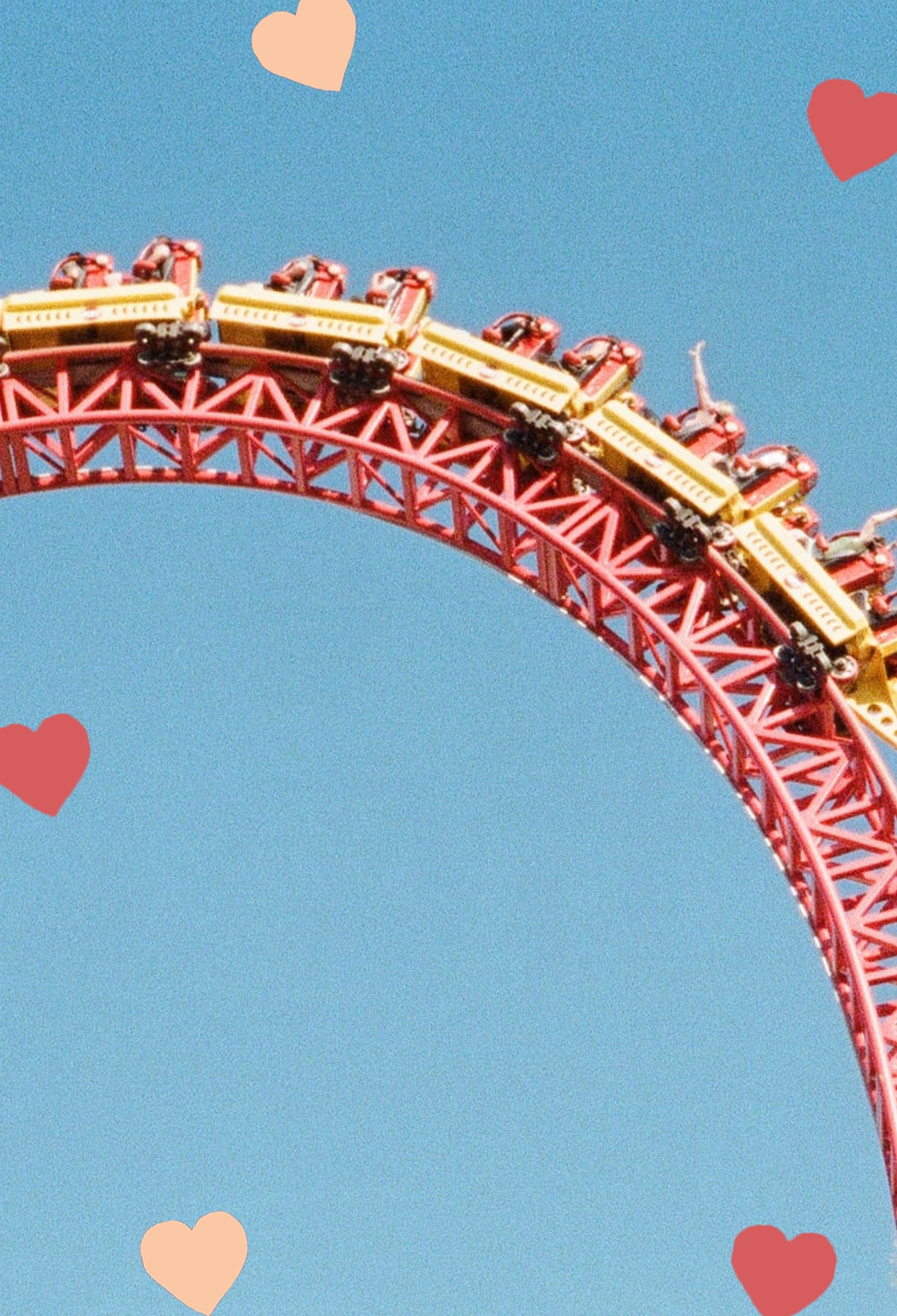 shot of gold coast rollercoaster, in red and yellow, against blue sky. people sit in it with their arms up. scattered hearts decorate the image.
