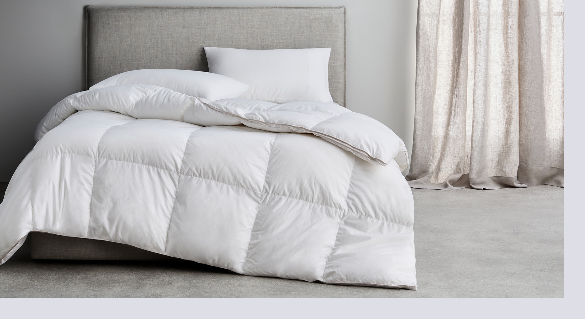 how to keep your bed warm in winter. feather and down quilt laid on bed with grey headboard, in room with grey walls and floor.