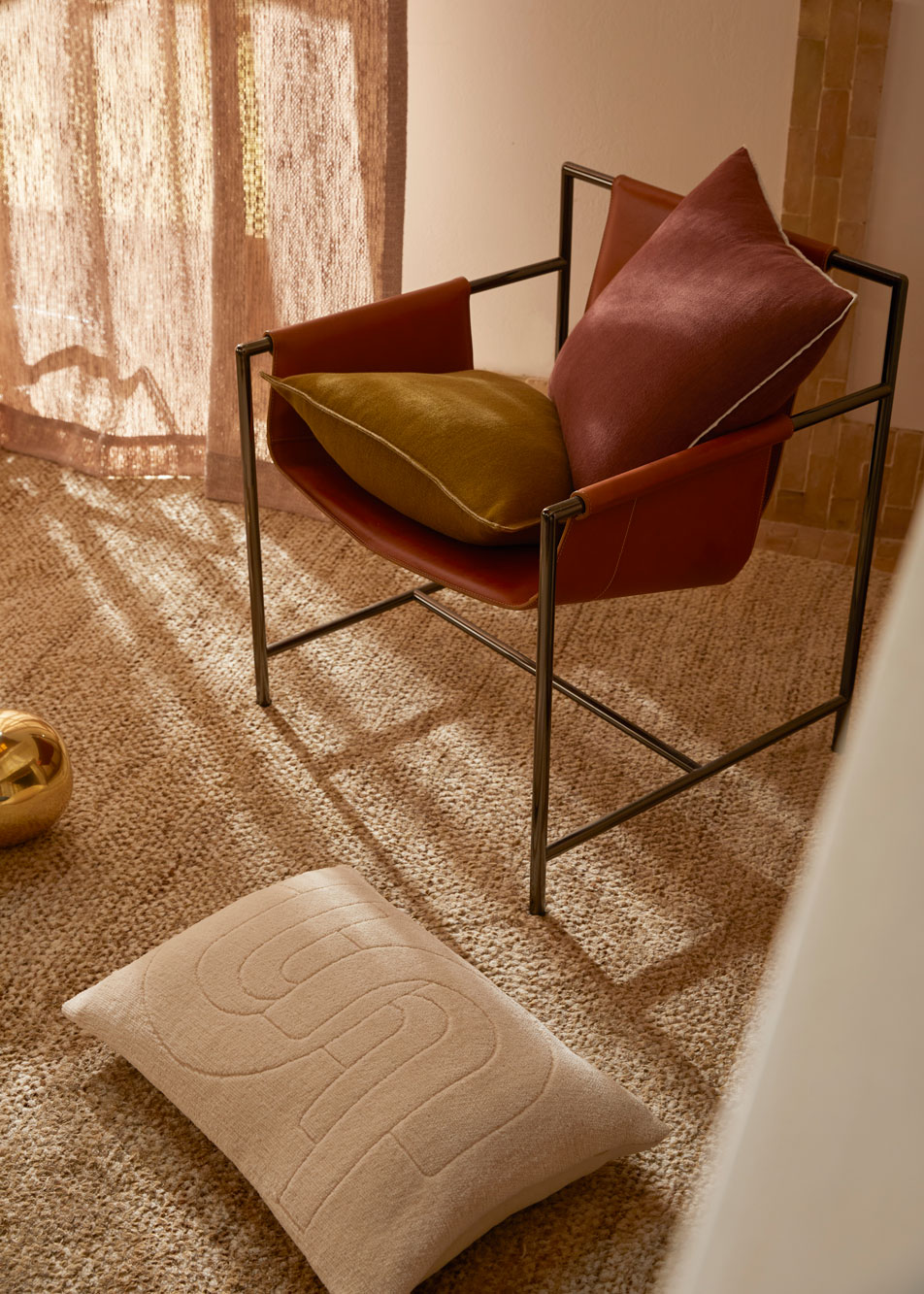 A leather chair with two cushions on it. Another cushion lays on the floor beside it.