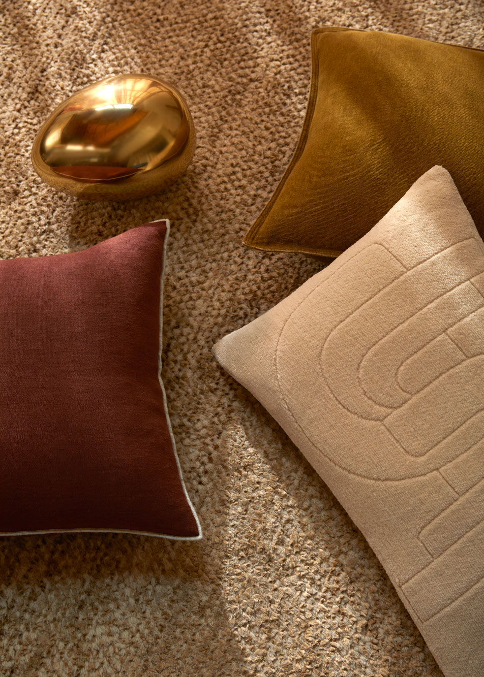 Three cushions in different colours laying on a rug, next to a golden metal sculpture