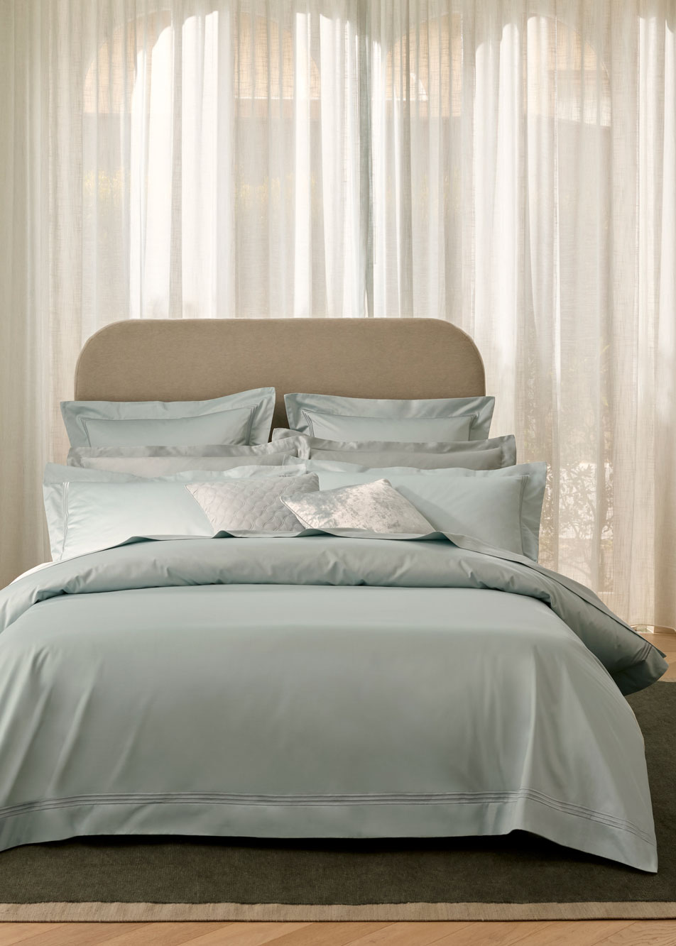 A bed with blue bed linen and a neutral fabric headboard