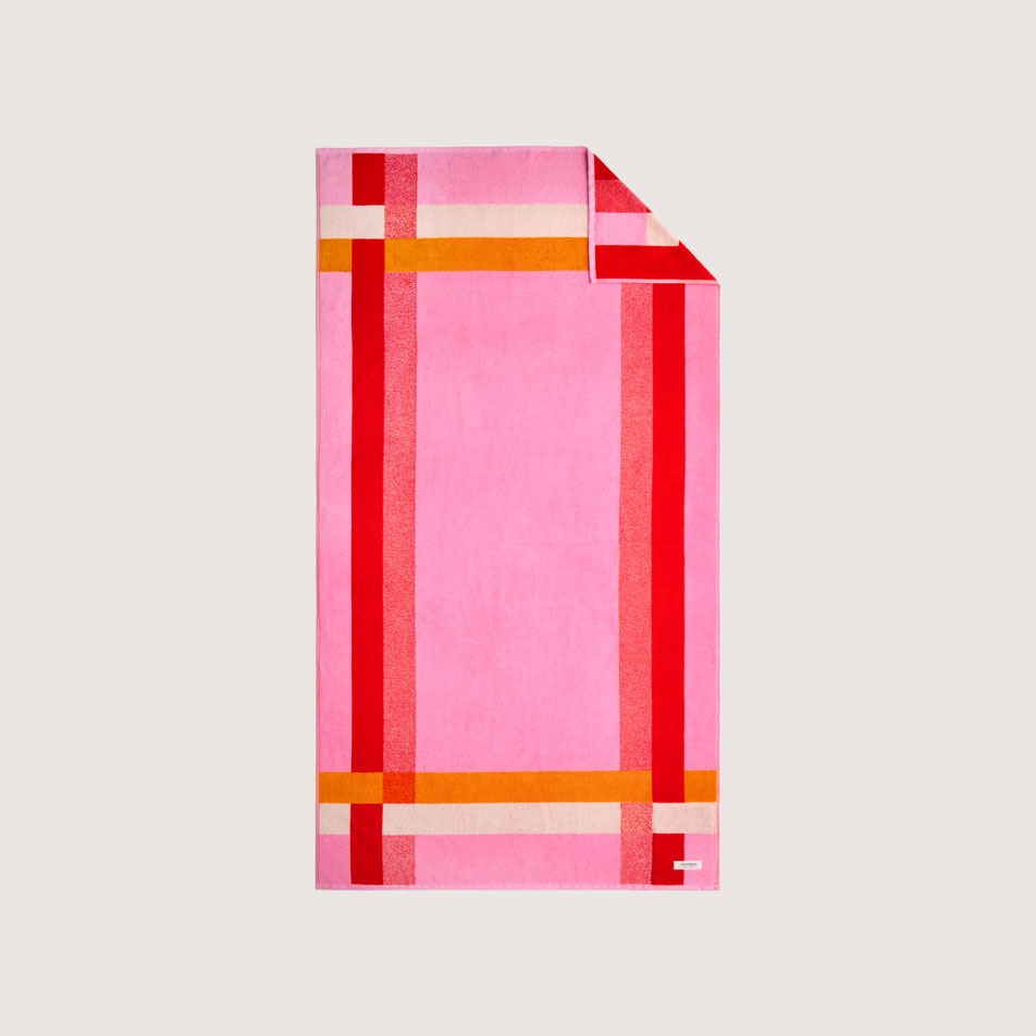 Flat lay photo of a vibrant pink beach towel with an orange and red frame pattern